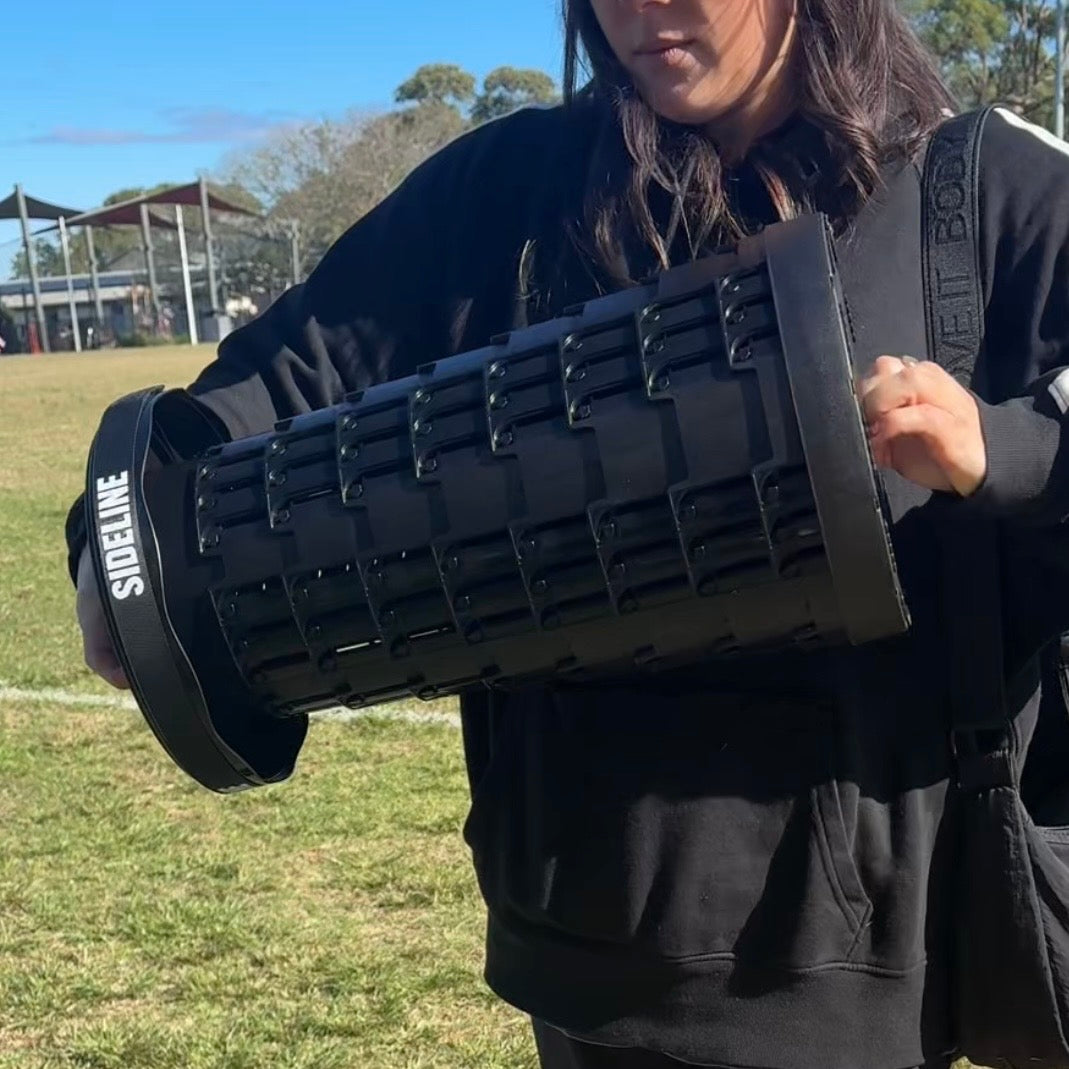 Collapsed Sideline Mini Luxe stool carried by hand at a sports ground